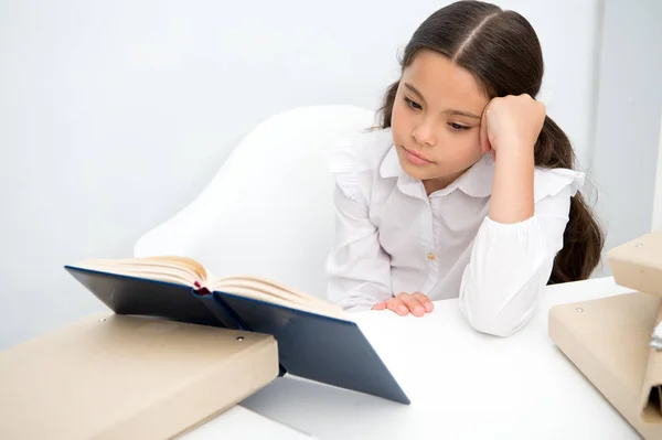 Czytanie książki nudne. Dziecko dziewczyna czyta książkę jednocześnie siedzieć Stół biały tło. Uczennica studia i czytanie książki. Dziecko dziewczynka Szkoła uniform znudzony obojętny niestety czytać nudna literatura — Zdjęcie stockowe