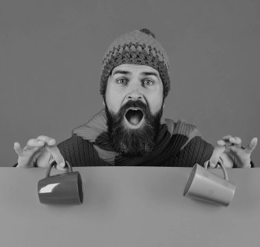 Sakallı kahverengi ve yeşil su bardağı tutar. Adam şaşırmış yüzü ile kahve fincanı tutarak sıcak şapka giyer