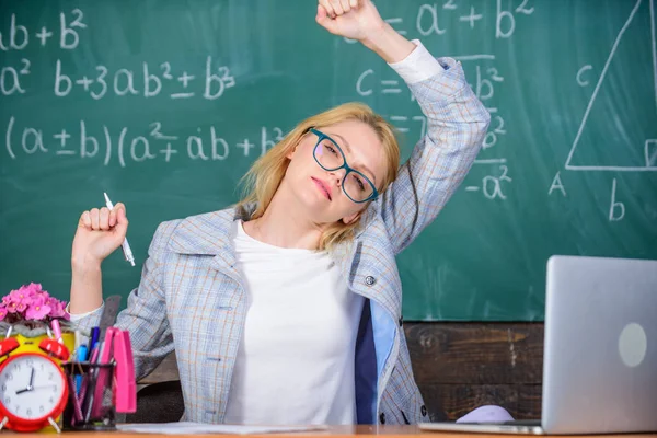 Latihan untuk menjaga kelincahan. Guru wanita duduk meja kelas latar belakang papan tulis. Regangkan dan lakukan latihan untuk meningkatkan kelincahan dan mendapatkan muatan energi. Bekerja jauh melampaui hari sekolah yang sebenarnya — Stok Foto