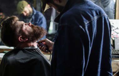 Sakal hipster istemcisinin, ayna yansıma arka plan üzerinde damat ile meşgul berber. Sakallı hippi cape kırpma şık berber dükkanı olarak profesyonel kuaför tarafından kaplı. Damat kavramı