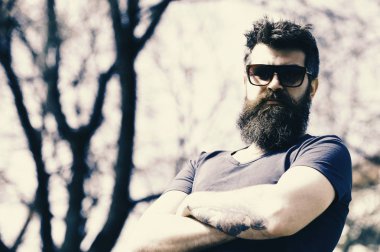 Ciddi bir yüz ayakta çapraz kollu adamla portresi. Acımasız adam uzun sakal ve bıyık güneşli kentsel sahnesinde trendy Eyewear