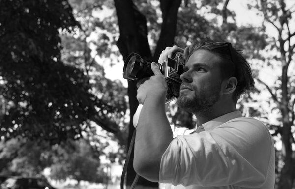 Man with beard holds photocamera on green park background. Photography concept. Photographer holds retro camera with big lense.