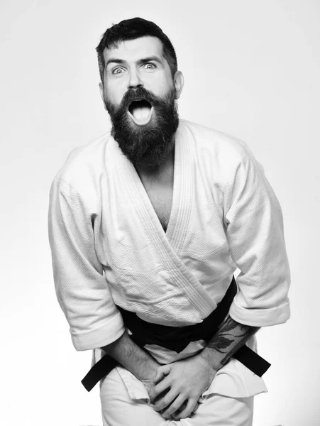 Karate hombre con cara de sufrimiento en uniforme. Hombre con barba en kimono blanco sobre fondo blanco —  Fotos de Stock