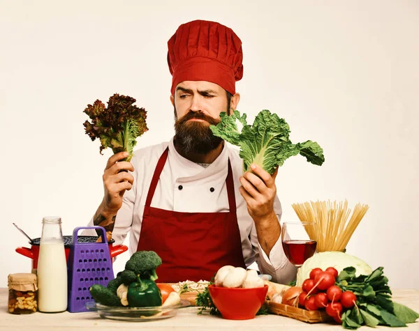 Chef with vegetables on white background. Male cook with grumpy face holding fresh lettuce.