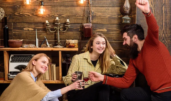 Company of friends celebrate with mulled wine in cozy atmosphere, wooden background. Cheers concept. Man and ladies on cheerful faces have fun together. Friends talking and celebrating with drinks