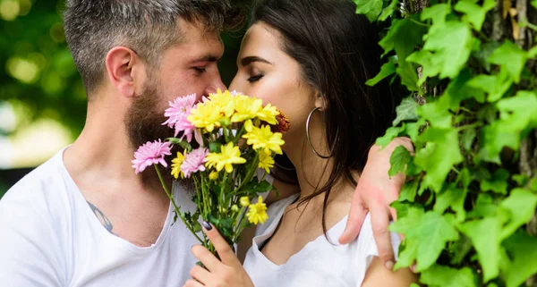 Man bearded hipster kisses girlfriend. Secret romantic kiss. Love romantic feelings. Moment of intimacy. Couple in love hiding behind bouquet flowers kiss. Couple love romantic date nature background — Stock Photo, Image