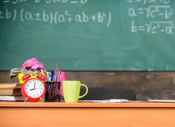 Kondisi kerja yang harus dipertimbangkan calon guru. Meja dengan perlengkapan sekolah buku jam alarm dan latar belakang papan tulis kelas mug. Guru tradisional tempat kerja. Atribut guru — Stok Foto