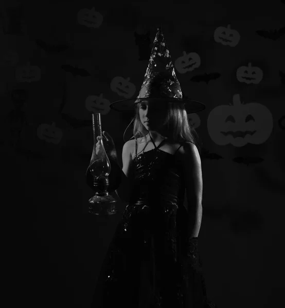 Kind in spooky heksen kostuum houdt gas lamp. Kleine heks dragen zwarte hoed. Meisje met nieuwsgierig gezicht — Stockfoto