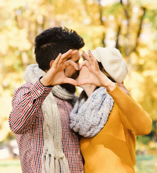 Hombre y mujer con rostros románticos se besan en el fondo de los árboles de otoño, primer plano de pareja haciendo forma de corazón con las manos — Foto de Stock