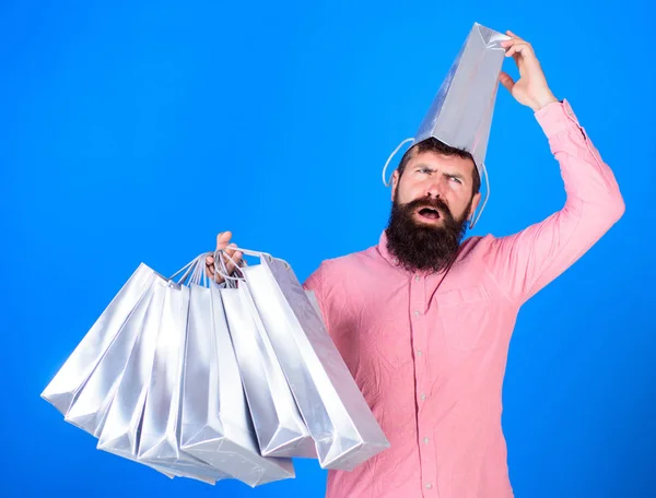 Mann mit Bart und Schnurrbart trägt Einkaufstaschen, blauer Hintergrund. Typen, die in der Verkaufssaison mit Rabatten einkaufen. Einkaufskonzept. Hipster mit Plastiktüte auf dem Kopf ist kaufsüchtig — Stockfoto