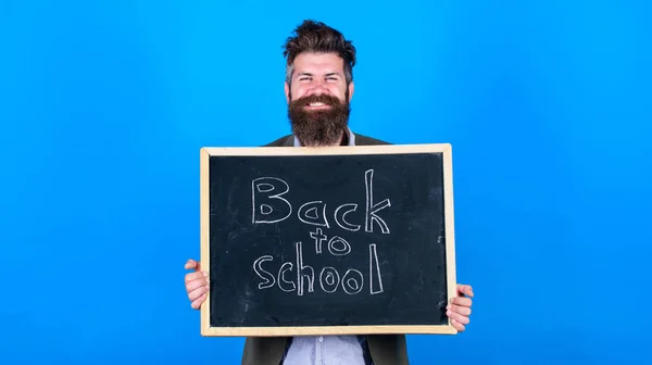 Új szemeszter az iskolában. Tanár szakállas ember áll, és tartja tábla felirattal vissza az iskola kék háttér. A tanár felkéri, hogy folytassa a tanulást. Folytasd velünk az oktatást. — Stock Fotó