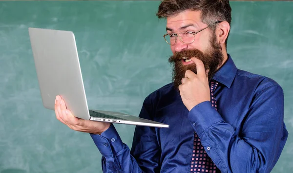 Hipster teacher wear eyeglasses and necktie holds laptop surfing internet. Teacher bearded cunning man modern laptop surfing internet chalkboard background. Interesting information. School lifehack — Stock Photo, Image