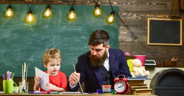 Çizim ders kavramı. Öğretmen sakal, baba ve küçük oğul çizerken, sınıfta oluşturma, kara tahta arka plan ile. Çocuk ve resim, çizim meşgul yüzleri öğretmen