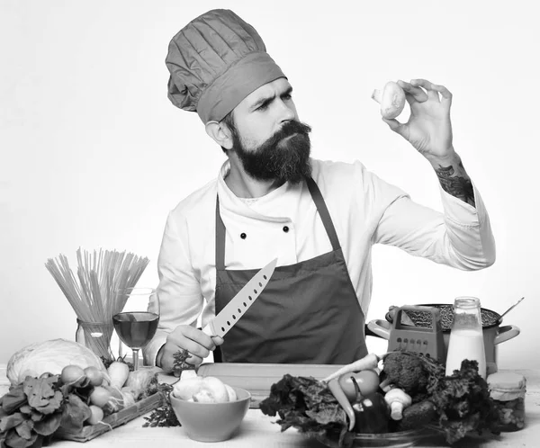 Cooking process concept. Chef prepares meal. Man with beard hold mushroom and knife on white background.