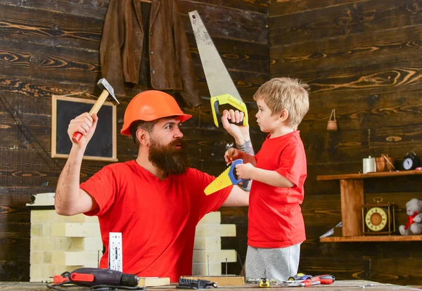 Baba, üst koruyucu kask öğretim oğlu okul atölyesinde farklı araçları kullanmaya sakallı. Evlat, neşeli çocuk oyuncak testere, baba ile handcrafting sırasında eğlenmek tutar. Babalık kavramı