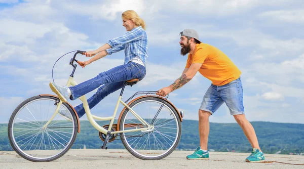 Kobieta jedzie rower na tle nieba. Dziewczyna jazda na rowerze, podczas gdy człowiek wspierać ją. Człowiek pomaga utrzymać równowagę jazdy rowerem. Serwis rowerowy. Serwis i pomoc. Mechanik pomaga utrzymać rower. Usługi wspomagające — Zdjęcie stockowe