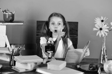 Kız fikri vardır ve kitap tutar. Kız öğrenci renkli Kırtasiye, kitap ve mikroskop ile masa başında oturur