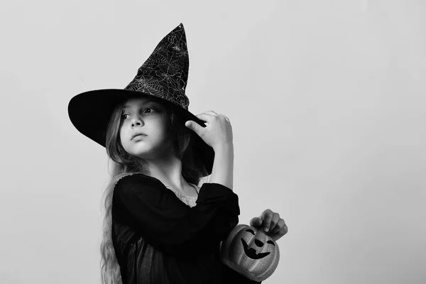 Kind in heks kostuum en jack o lantern. Kid in zwarte heks hoed, jurk en geconcentreerde gezicht — Stockfoto