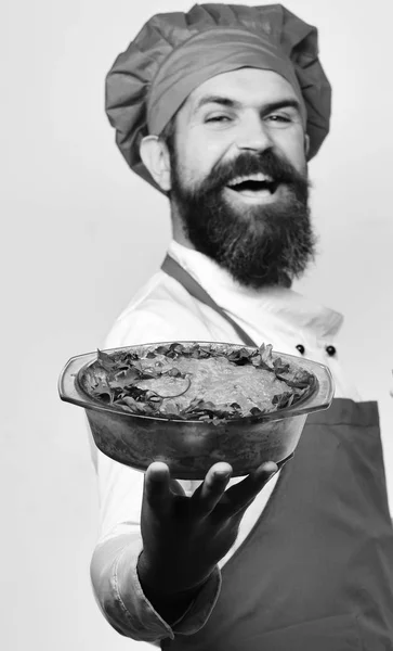Концепция кулинарного и диетического питания. Человек с бородой изолирован на белом фоне. Шеф держит запеканку. — стоковое фото
