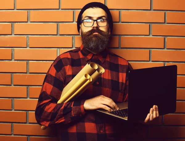 Bearded brutal caucasian hipster holding laptop and craft paper — Stock Photo, Image