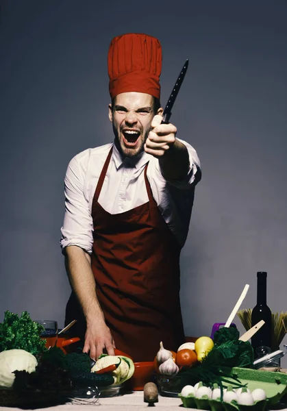 Chef-kok in Bourgondië uniforme bereidt voedsel. Man met baard in de keuken op een grijze achtergrond. — Stockfoto