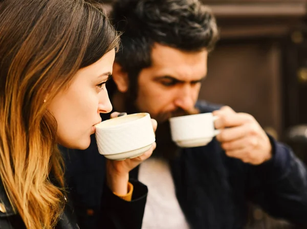 Девушка и бородатый парень пьют кофе на фоне коричневой террасы. Пара влюбленных пьет эспрессо во время кофе-брейка . — стоковое фото