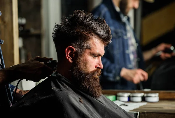 Hand of barber with hair clipper, close up. Hipster bearded client getting hairstyle. Barbershop concept. Man with beard in hairdressers chair, salon background. Barber works with hair clipper — Stock Photo, Image