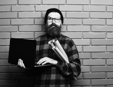 Kaba sakallı, beyaz tenli hippi elinde dizüstü bilgisayar ve el işi kâğıdı tutuyor.