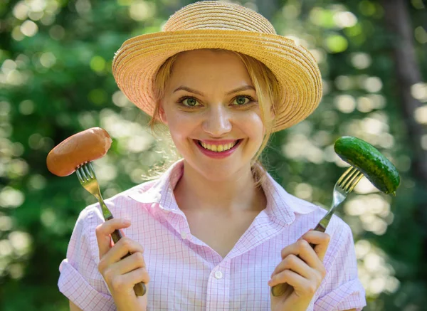 Choice between meat or vegetables. Girl smiling face holds forks with sausage and cucumber. Alternative nutrition for vegetarians. Vegetarians nutritional choice. Vegetarian lifestyle is her choice