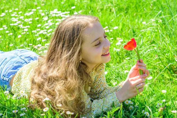 子供は、草原に横たわっている間チューリップの香りをお楽しみください。草地、草背景に横になっている長い髪を持つ少女。幸せそうな顔の女の子は、日当たりの良い春の日の赤いチューリップの花を保持します。アレルギーの概念 — ストック写真