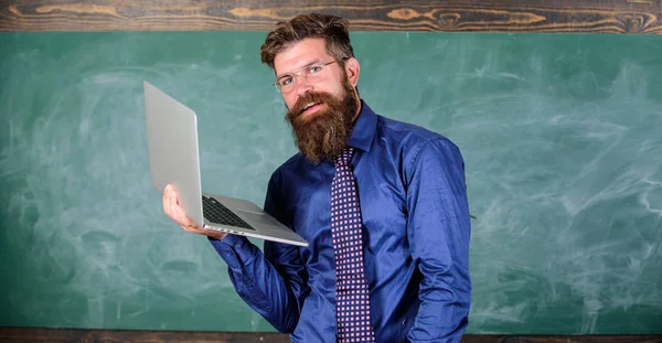 Hipster profesor usar gafas y corbata sostiene portátil navegar por Internet. Concepto de educación a distancia. Profesor barbudo hombre con portátil moderno navegar fondo pizarra de Internet. Navegación por Internet —  Fotos de Stock