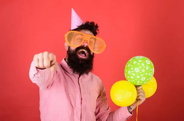 Hippi dev güneş gözlüğü Doğum günü kutluyor. İleriye dönük parti şapkalı adam. Doğum günü partisi konsepti. Sakal ve bıyık mutlu yüz tutan grup hava balonları, kırmızı arka plan üzerinde olan adam — Stok fotoğraf