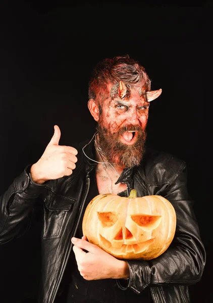 Man wearing makeup holds pumpkin on black background. Devil or monster with October decorations. Halloween party concept. — Stock Photo, Image