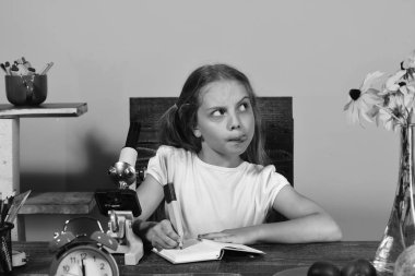 Kız saat, mikroskop ve çiçekler ile masasında oturuyor. Yüz sorgulama ile kız öğrenci not defterinde yazıyor