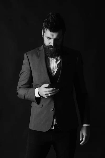Geschäfts- und Technologiekonzept. Geschäftsmann mit Bart hält Handy in der Hand. Mann im schicken Anzug — Stockfoto