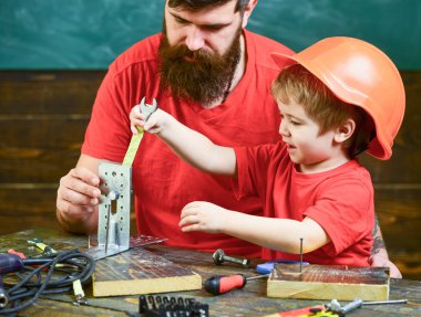 Sınıfta, arka plan kara tahta araçlarını kullanmak için küçük oğlu öğretim sakallı baba. Takım iş kavramı. Evlat, Çocuk koruyucu kask meşgul el ile onarma yapar, babamla aletlerle çalışırız