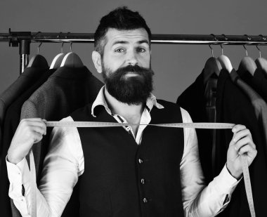 Tezgâhtar veya kaset elinde ölçme ile satıcı. Ceket mavi zemin üzerine yakındaki merak yüz ile iş adamı. Yeleği giysi raf tarafından sakallı adam. Tüketicilik ve zarafet kavramı.