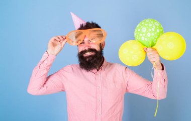 Hipster dev gözlük içinde Doğum günü kutluyor. Parti öznitelikleri kavramı. Hava balonları ile parti şapkalı adamı kutluyor. Mutlu yüz tutun hava balonları, açık mavi renkli sakallı