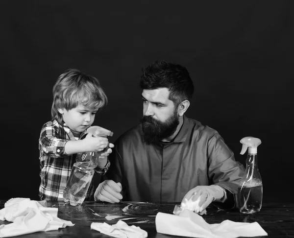 Kid and father with busy faces cleaning together with spray. Man with cute child on black background.