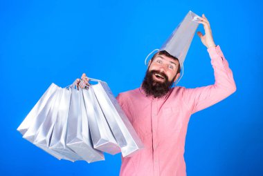 Adam sakal ve bıyık taşır alışveriş torbaları, mavi arka plan ile. Alışveriş kavramı. Kafasında torba ile sürpriz yüzündeki hipster bağımlısı Alışverişkoliğin var. Adam satış sezon indirimleri ile alışveriş