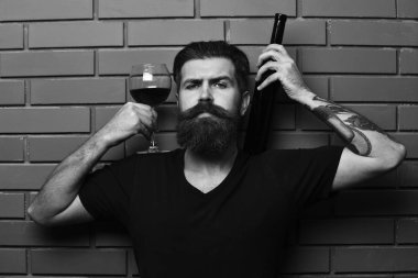 Sakallı adam alkollü içecek tuğla duvar arka plan üzerinde tutar. Kırmızı cabernet veya merlot maço emin yüz sunar.