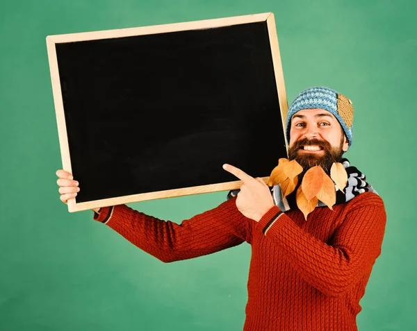 Guy holds chalkboard at barbershop, copy space. Man in warm hat holds blackboard on green background