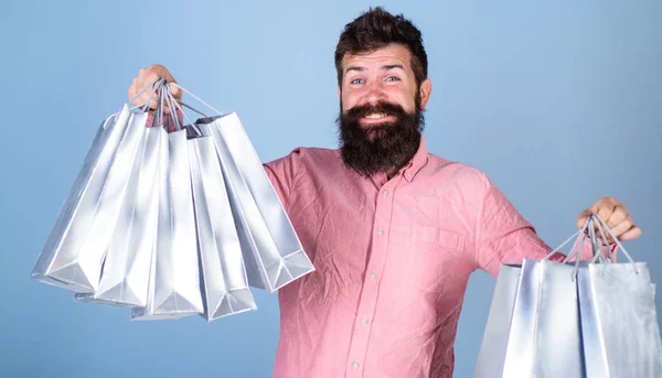 Concept de vente et de remise. Guy magasinant sur la saison des ventes avec des réductions. Hipster sur le visage heureux est accro au shopping ou accro au shopping. Homme avec barbe et moustache tenir des sacs à provisions, fond bleu clair — Photo