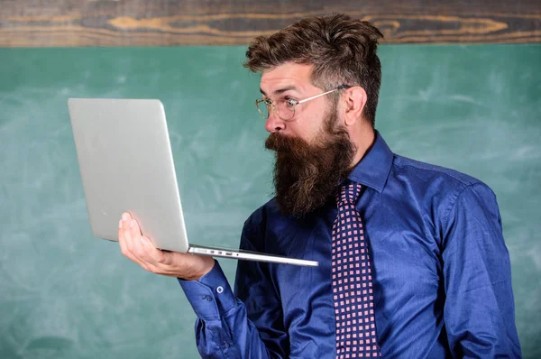 Hipster profesor usar gafas y corbata sostiene portátil navegar por Internet. Una noticia impactante. Profesor barbudo sorprendido hombre con portátil moderno navegar fondo pizarra de Internet. Información impactante —  Fotos de Stock