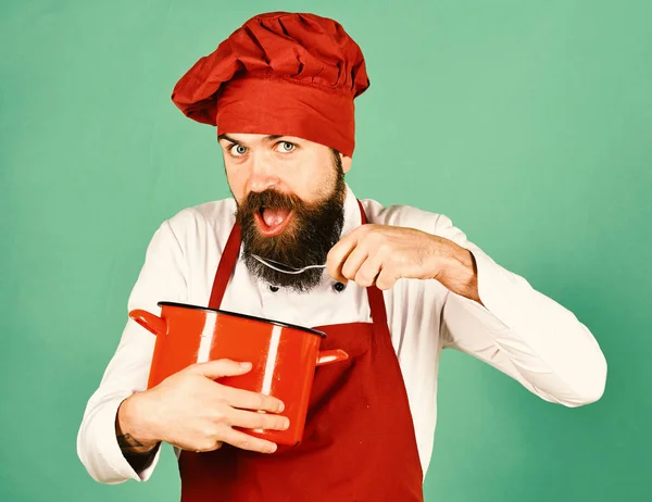 Koken met hongerige gezicht in Bourgondië hoed en schort houdt pot en lepel. Man met baard houdt keukengerei op groene achtergrond — Stockfoto