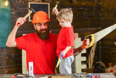 Evlat, neşeli çocuk oyuncak testere, baba ile handcrafting sırasında eğlenmek tutar. Baba, üst koruyucu kask öğretim oğlu okul atölyesinde farklı araçları kullanmaya sakallı. Babalık kavramı