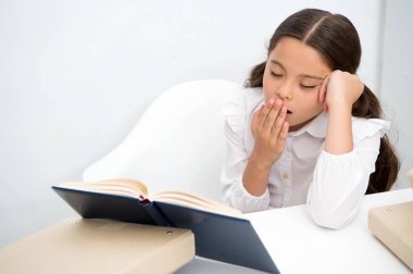 Edebiyat sıkıcı. Kız çocuk sit tablo beyaz arka planı süre kitap okur. Kız öğrenci eğitim ve kitap okumak. Çocuk kız okul üniforması sıkılmış esneme yüz ne yazık ki sıkıcı edebiyat okumak. Yorucu görev.