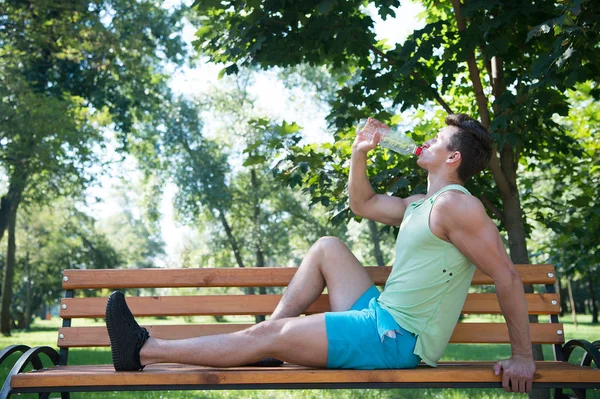 Drink water concept. Sportsman drink water on bench. Young man drink water after training on fresh air. Athletic guy drink water from plastic bottle in park