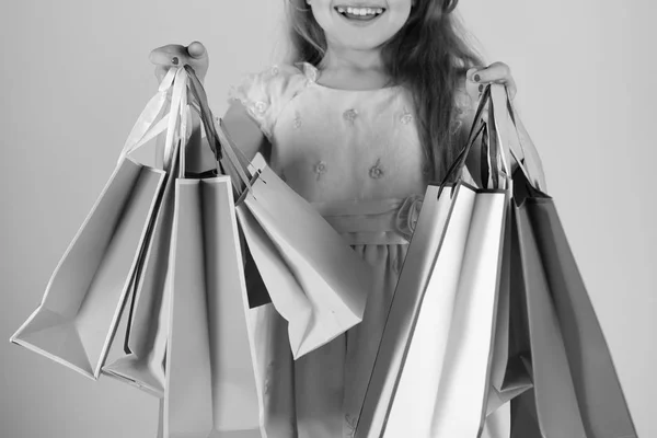Έννοια shopaholic και παιδική ηλικία. Κυρία αγοραστής στο φόρεμα, κυματιστά μαλλιά. Το κορίτσι κρατά τσάντες για ψώνια — Φωτογραφία Αρχείου