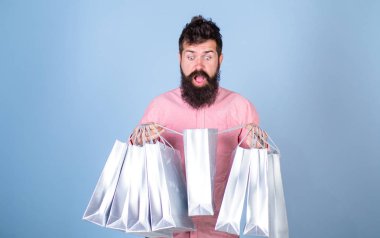 Şok yüz bağımlısı alışveriş veya Alışverişkoliğin hippi. Satış sezon indirimlerle alışveriş adam. Sakal ve bıyık taşımak alışveriş torbaları, açık mavi renkli olan adam. Satış ve indirim kavramı